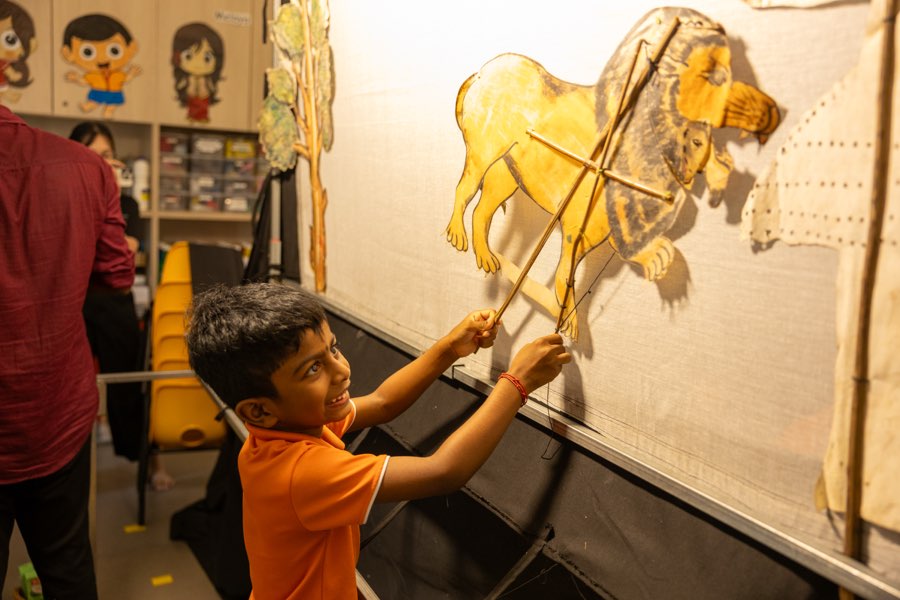 A boy working a leather shadow puppet against the screen